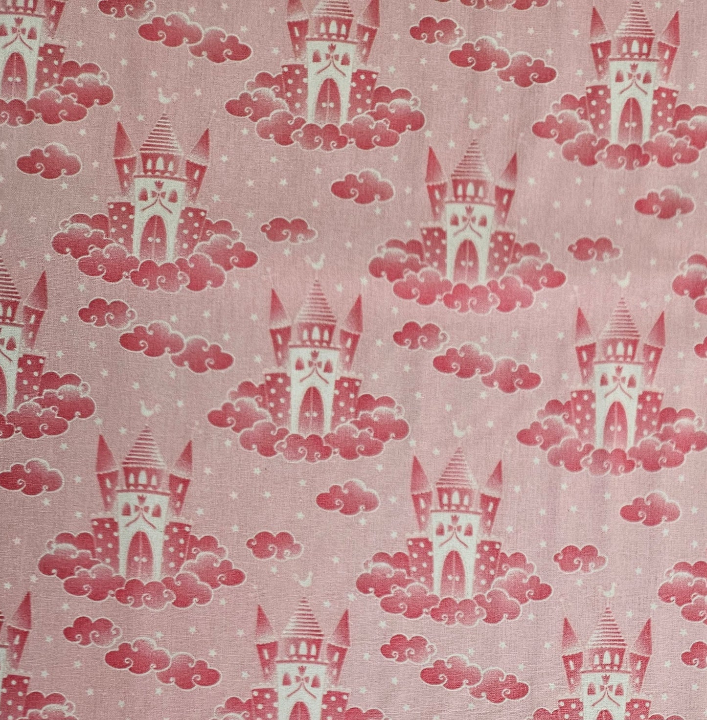 A close-up of a pink fabric with a repeating pattern of red castles rising from pink clouds, with small white stars scattered throughout.
