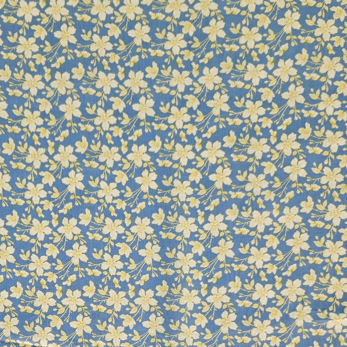 A close-up of a fabric or wallpaper pattern featuring a dense, repeating print of small yellow flowers and green stems on a medium blue background.