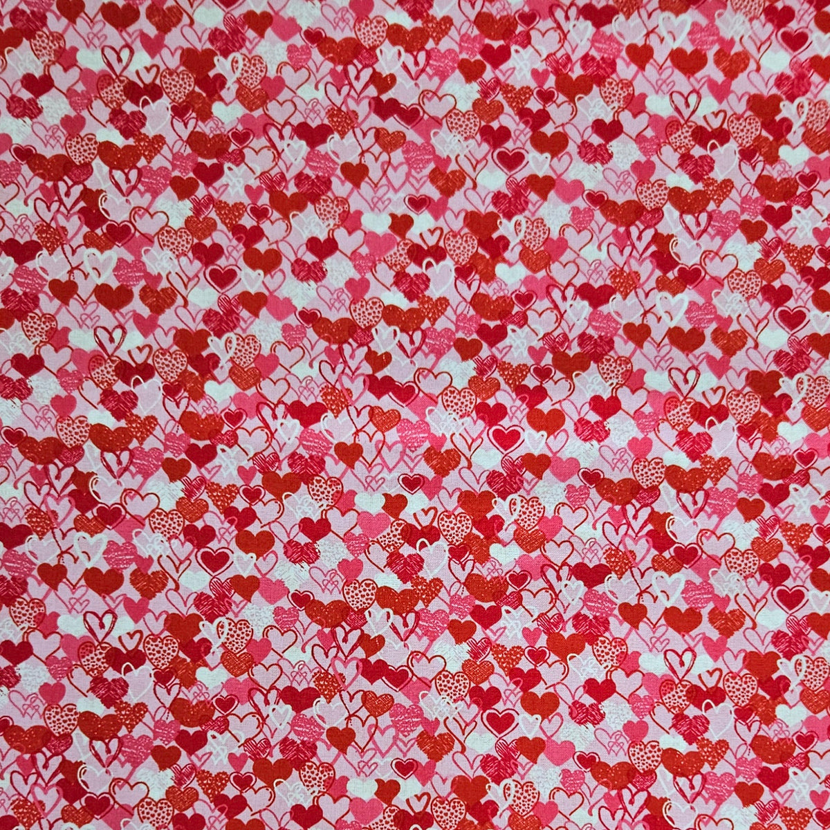 A close-up of a fabric or material swatch featuring a dense pattern of red, pink, and orange hearts on a white background.