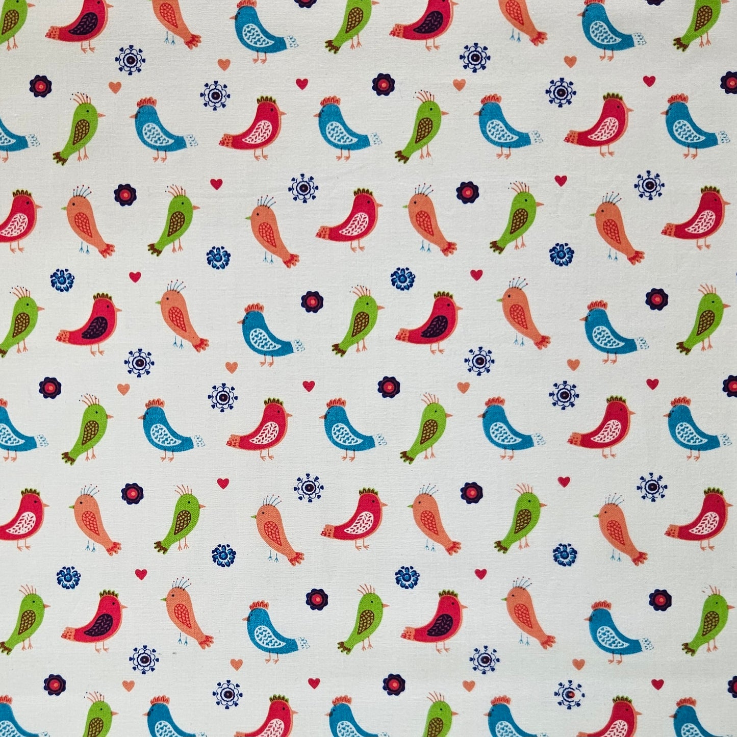 A close-up of a fabric pattern featuring colourful stylized birds in red, blue, green, and orange on a warm white background, accented with small red hearts and dark blue floral motifs.