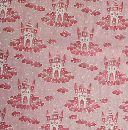 A close-up of a pink fabric with a repeating pattern of red castles rising from pink clouds, with small white stars scattered throughout.