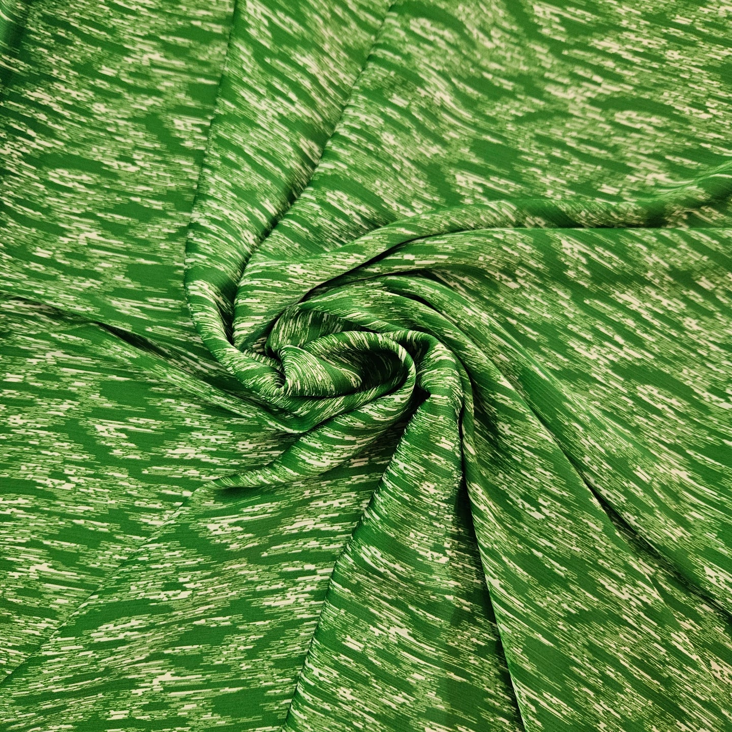 A close-up of a green fabric with a textured, heathered pattern, arranged in a spiral drape to show its texture and flexibility.