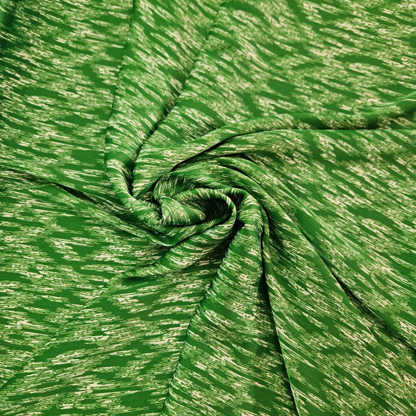 A close-up of a green fabric with a textured, heathered pattern, arranged in a spiral drape to show its texture and flexibility.