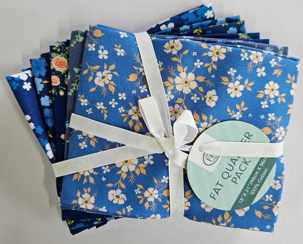 A bundle of folded patterned fabric squares tied with a white ribbon and a round paper tag that reads 'FAT QUARTER PACK,' photographed on a plain light background.
