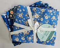 A bundle of folded patterned fabric squares tied with a white ribbon and a round paper tag that reads 'FAT QUARTER PACK,' photographed on a plain light background.