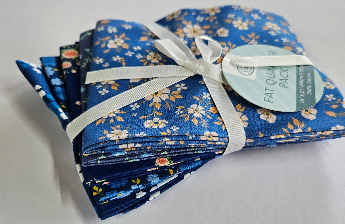 A folded bundle of blue patterned fabric pieces tied with a white ribbon and a round paper tag, placed on a plain white surface.