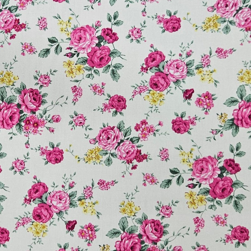 A close-up of a floral fabric pattern featuring pink and magenta roses, yellow blossoms, and green leaves on a light cream background.